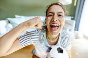 Young woman holding soccer ball and cheering for her sports team